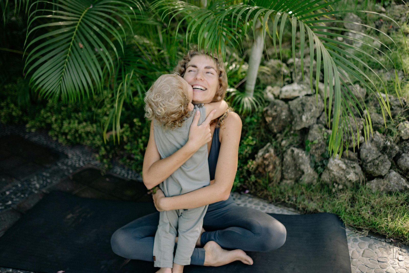 Happy mother and child enjoying a warm embrace outdoors on a yoga mat with nature around.